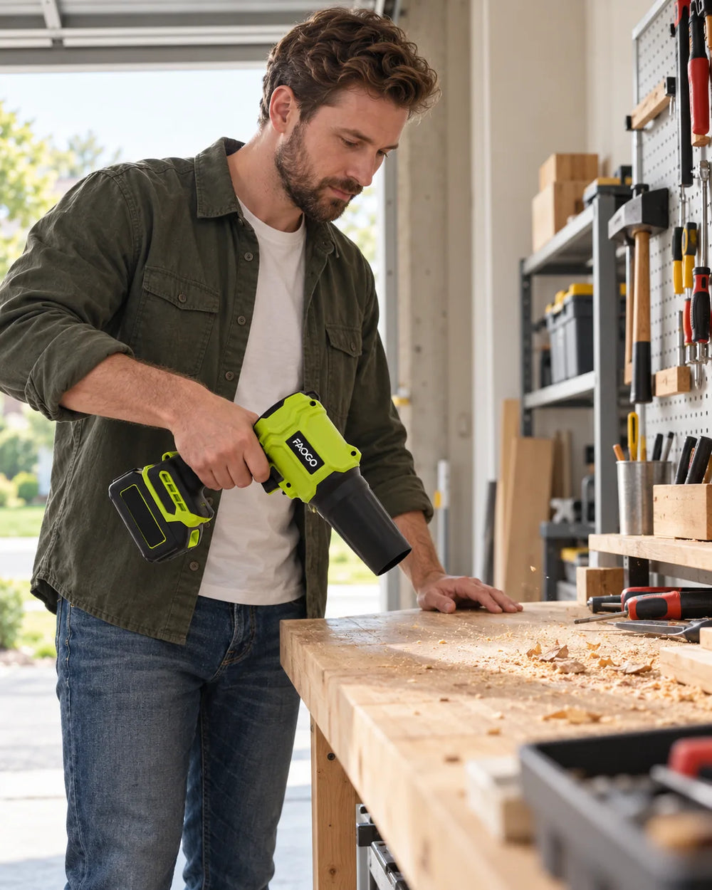 Man using a green FAOGO blower to clear loose debris from a garage workbench